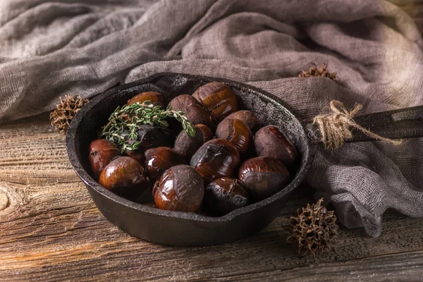 Kestane. Koyu ahşap masa üzerinde dökme demir tavada kavrulmuş yenilebilir kestane hizmet.