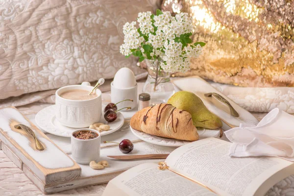 Romantic breakfast in bed with coffee, croissants, cherries and flowers.