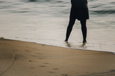 Sahilde sakince kumsala vuran adamın ayakları deniz suyunda.