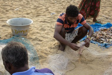 CHENNAI, TAMIL NADU, INDIA - CIRCA AY YIL - Balıkçılar sahilde oturur ve ağlarındaki balıkları söker ve sabahları Marina sahilinde satarlar.