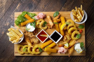 Kızarmış karides, kalamar, sosları, patates kızartması ile ahşap bir tahta. Fast food. Koyu arka plan