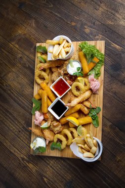 Kızarmış karides, kalamar, sosları, patates kızartması ile ahşap bir tahta. Fast food. Koyu arka plan