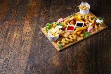 Kızarmış karides, kalamar, sosları, patates kızartması ile ahşap bir tahta. Fast food. Koyu arka plan