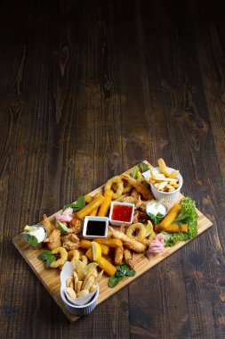 Kızarmış karides, kalamar, sosları, patates kızartması ile ahşap bir tahta. Fast food. Koyu arka plan