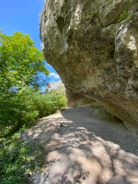 summer day, mountain path under the rock against the background of the sky and clouds