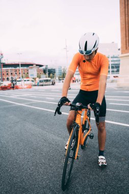 Genç adam bisiklet gezisine hazırlanıyor. Turuncu bir bisikleti ve beyaz bir kaskı var.. 