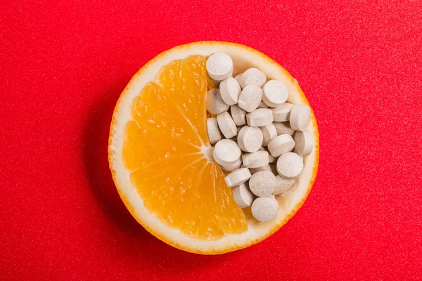 Comprimidos com vitaminas em uma fatia de laranja em um fundo vermelho . — Fotografia de Stock
