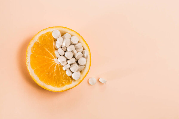 Таблетки с витаминами в апельсиновом ломтике на бежевом фоне
.