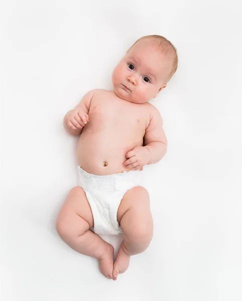 Una linda niña de cuatro meses con una cubierta de pañal blanca se acuesta sobre un fondo blanco . —  Fotos de Stock