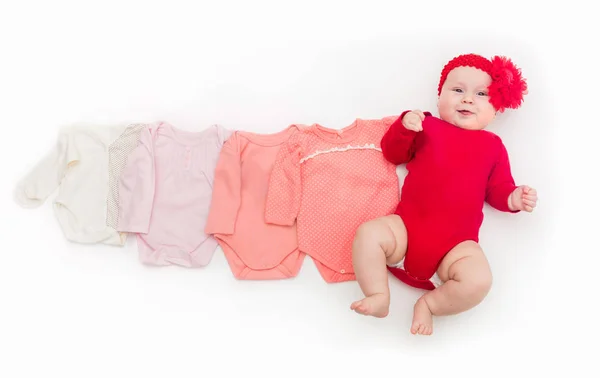 Un bebé feliz de cuatro meses en traje de cuerpo rojo acostado sobre un fondo blanco con ropa rosa de menor tamaño . — Foto de Stock