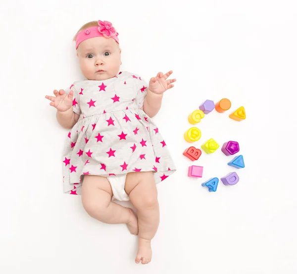 Retrato de una niña dulce con un vestido rosa y un lazo de diadema, aislado en blanco en el estudio con el número seis de juguetes — Foto de Stock