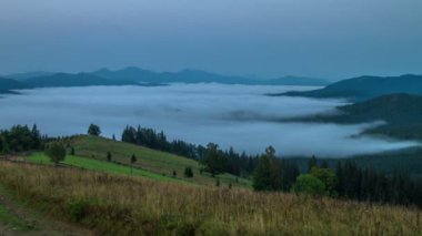 Misty sabah yalnız ağaç ve toprak yol ön planda dağlar ve sis ile bulutlar içinde belgili tanımlık geçmiş. Timelapse.