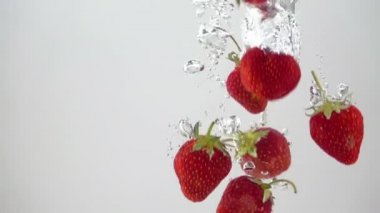 Olgun Çilekler Suya dökülüyor. Işık Arkaplanı. Yavaş Hareket.