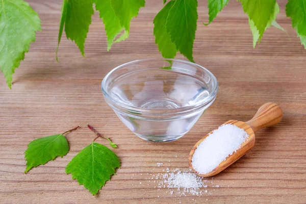 Natural mouthwash bowl with xylitol water and wood scoop with birch sugar and leafs on wooden — Stock Photo, Image