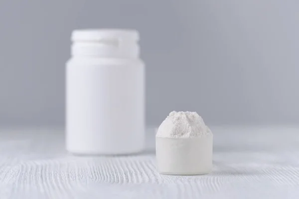 A scoop with white powder closeup and a jar on gray background — Stock Photo, Image