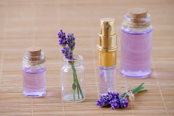 Levandulová voda a olej ve skleněných lahvích a čerstvé levandulové květy na dřevěné pozadí — Stock fotografie