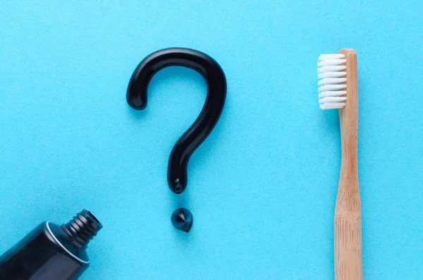 Question from black toothpaste, teeth care concept, wooden toothbrush on blue background — Stock Photo, Image