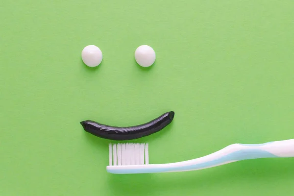 Лицо с улыбкой из белой и черной зубной пасты, концепция ухода за зубами, зубная щетка на зеленом фоне — стоковое фото