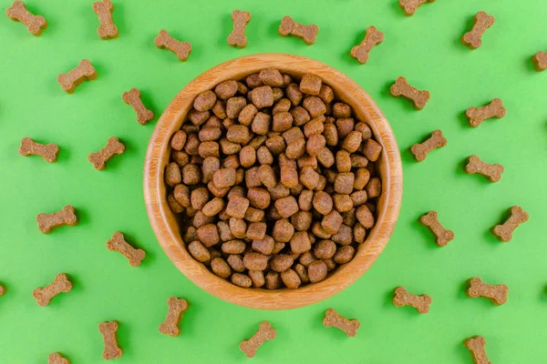 dog food in a bowl and snack like bones on green background, flat lay