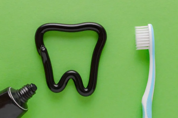 Зуб из черной зубной пасты, концепция ухода за зубами, зубная щетка на зеленом фоне — стоковое фото
