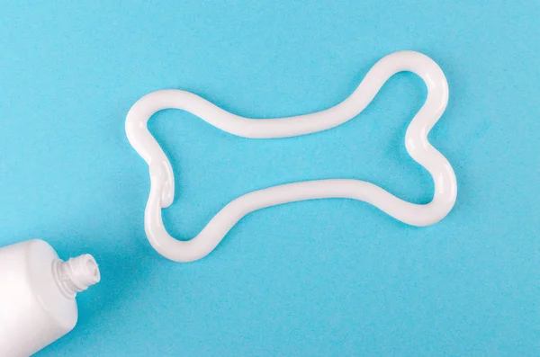 Кістка з білої зубної пасти, концепція догляду за зубами тварин, на синьому фоні — стокове фото