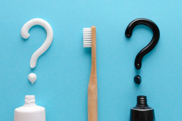问题从白色和黑色牙膏，牙齿护理概念，蓝色背景的木制牙刷 — 图库照片