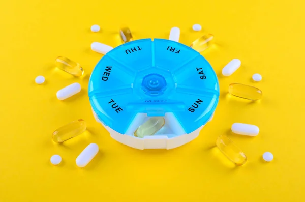 Různé léky, Omega tobolky, jeden týden a modré tabletky na žlutém pozadí — Stock fotografie