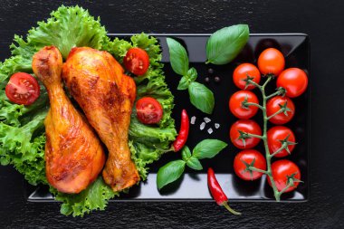 taze domates, basilik ve siyah arka plan üzerinde biber ile sağlıklı ızgara tavuk bacakları