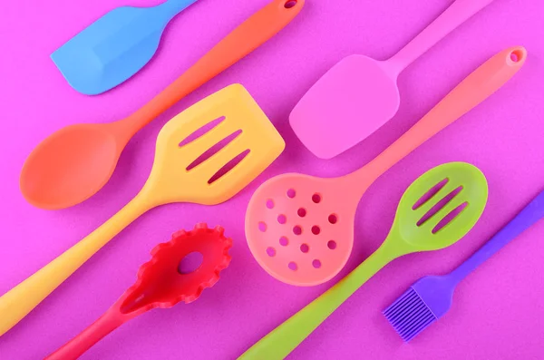 bright multi colored kitchen utensils on purple background