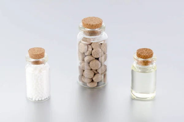 natural medicine bottles with herbal pills, globules and oil on gray background