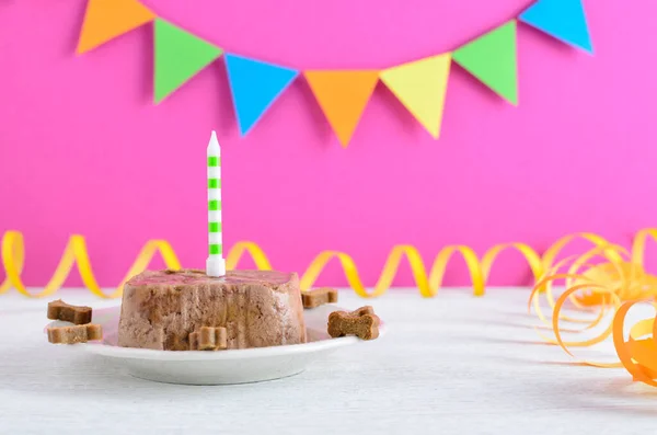 Happy birthday cake for dog from wet food and treats with candle on pink party background — Stock Photo, Image
