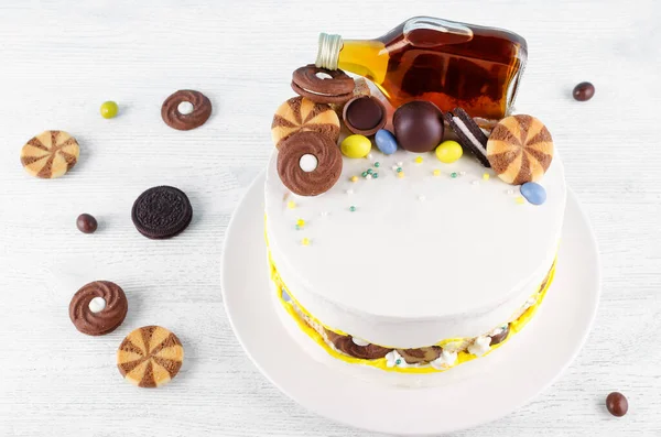 Rolig tårta med en flaska alkohol, godis och kakor på träbord — Stockfoto