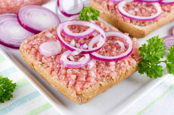 german food mett ground pork, bun and raw meat with onion and parsley, closeup