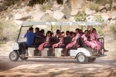 Pembe aynı elbiseler bir okul üniformalı genç kız öğrenciler bir el salla uzun elektrikli araç - golf arabası manzaraları doğru oluyor ve geçenler için gülümse. Hampi, 10 Ocak 2018 Tarih, Türkiye, İstanbul, yirmiden