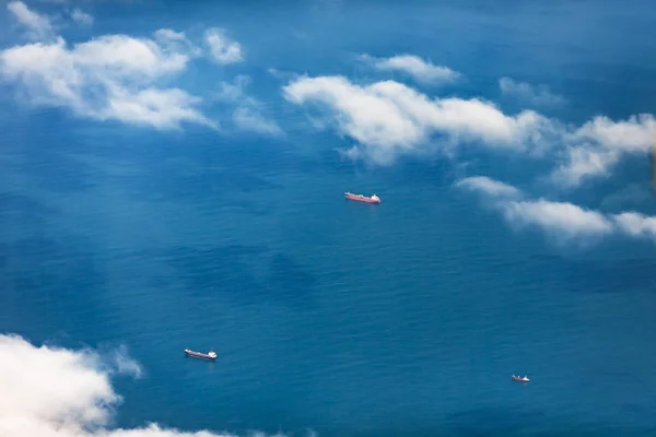 Aerial view through a veil of clouds on three cargoships floating in ocean waters.