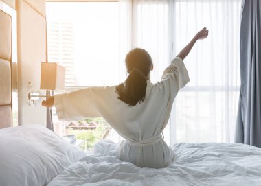 Kolay bir yaşam tarzı genç Asyalı kız sabah uyanıp dinleniyor. Tembel gün konsepti için otel odasında dinleniyor.