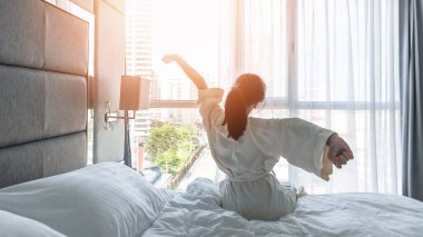 Otel odası konforu ve iyi bir uyku. Yatakta Asyalı bir kızın rahat yaşam tarzı. İyi bir sabah uyanıp, biraz dinlenmek. 