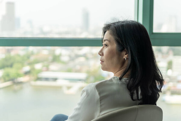 Женщина средних лет с современным образом жизни, счастливая концепция качества жизни с зрелой менопаузы женщины расслабляющий сидя в комнате отдыха отеля или роскошный номер с прекрасным видом на город