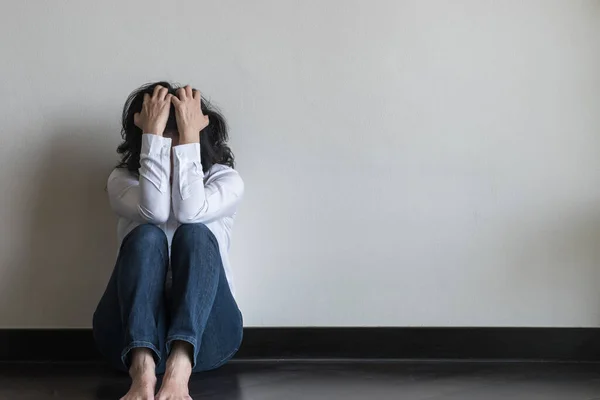 Panic attack woman, stressful depressed emotional person with anxiety disorder mental health illness, headache and migraine sitting feeling bad with back against wall on the floor in domestic home