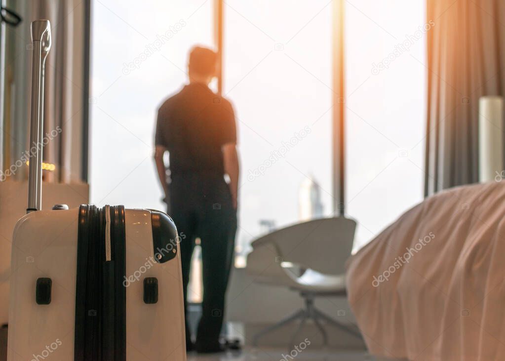 Luggage with blurred businessman in luxury hotel guest room looking out toward city view