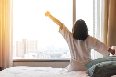 Kolay yaşam tarzı Asyalı bir kadın sabah uyanıp dinleniyor. Tembel gün konsepti için otel odasında dinleniyor.