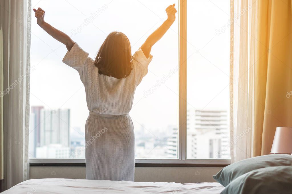 Easy lifestyle Asian woman waking up in weekend morning taking some rest relaxing in comfort city hotel room enjoying world lazy day, having happy life quality balance concept