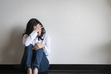 Stresli bir kadın duygusal bunalım ve endişe içinde evde oturma odasında beyaz bir duvarla oturuyor.  