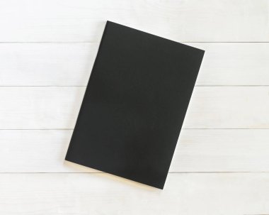 Kitap modeli boş siyah deri A4 boyutlu kapak şablonu beyaz ahşap masa üzerinde yatıyordu.