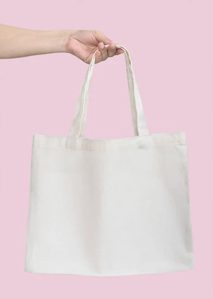 Tote bag canvas white cotton fabric cloth for eco shoulder shopping sack mockup blank template isolated on pastel pink background (clipping path) with woman's handling hand