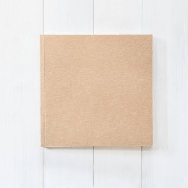 Boş kitap kare boyutunda katalog dergileri, broşür veya not kapağı şablonu geri dönüşüm kahverengi kağıt dokusu düz beyaz renkli ahşap tablo üzerinde yatıyordu