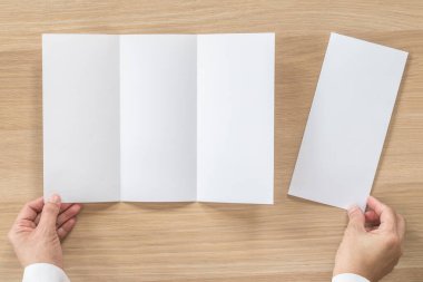 Üç katlı pamphelt broşür tasarımı. İş adamının elindeki A4 boyutlu kağıt. Şablon çizimi, ahşap masa üzerindeki düz çizgi.
