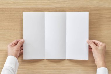 Üç katlı pamphelt broşür tasarımı. İş adamının elindeki A4 boyutlu kağıt. Şablon çizimi, ahşap masa üzerindeki düz çizgi.