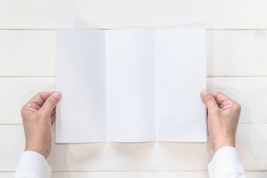 Boş broşür, üç katlı el ilanı A4 kağıt şablonu, iş adamının elinde, ahşap masa üzerinde, yukarıdan bakıldığında.