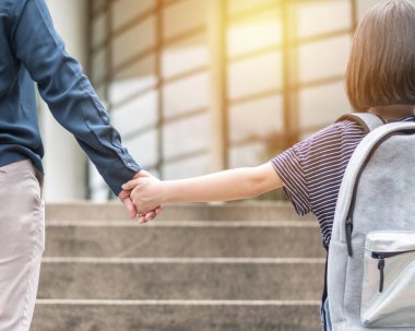Kız çocuğu (ilkokul öğrencisi) sırt çantasıyla annesinin elini tutuyor eğitim binasının merdivenlerinden çıkıp sınıfa gidiyor ilk gün okula dönüyor ve çocuğu işe getiriyor.
